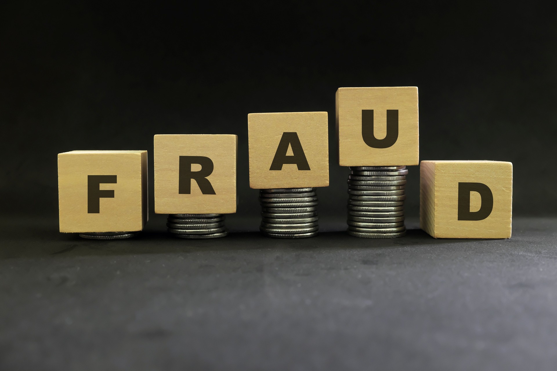 Investment scam, fraud and Ponzi scheme concept. Stack of coins on wooden blocks with word ponzi in dark black background.